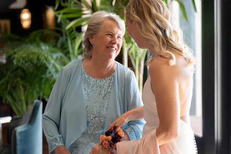 A woman in a sequined blue cardigan holds a small orange bouquet while speaking with a guest.