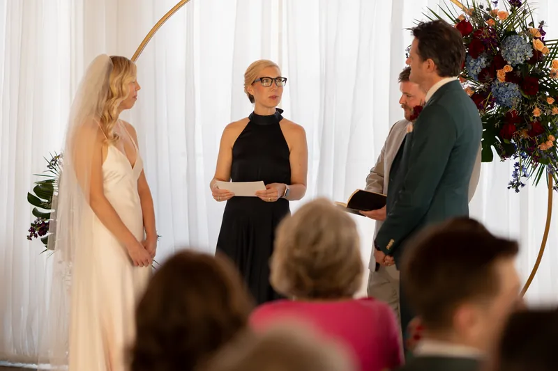 Kerry and Rhett exchange vows with the officiant while seated guests watch the ceremony beneath draped white fabric.