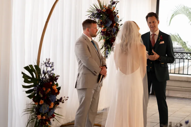 Rhett stands beside Kerry in a cream suit as an officiant speaks during their ceremony at Casa Monica Resort & Spa