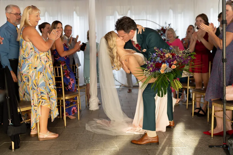 Kerry bends to embrace a guest while holding a vibrant bouquet of coral and green flowers during the recessional.