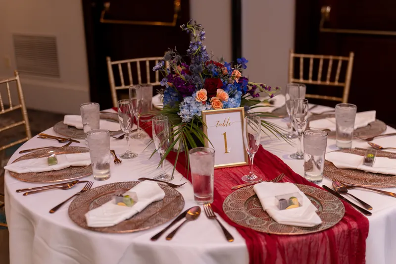 Table number one surrounded by blue and coral floral arrangement, with white plates and burgundy fabric runner at Casa Monica
