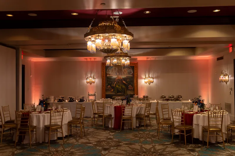 Elegant reception ballroom at Casa Monica Resort & Spa glows with amber uplighting, crystal chandelier, and round tables