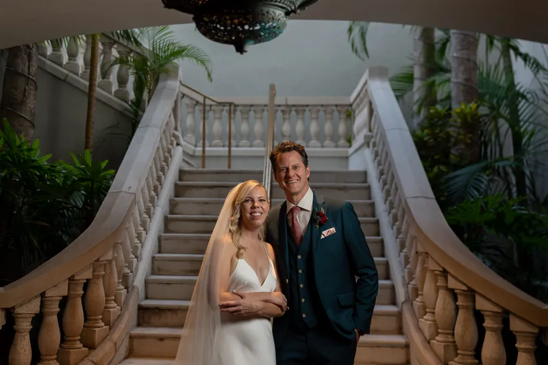 Kerry and Rhett walk down the grand staircase flanked by potted plants and decorative railings.