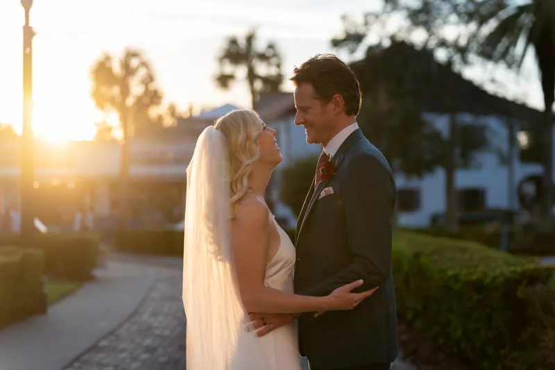 Kerry and Rhett embrace at sunset with palm trees and the resort's architecture framing the golden light.