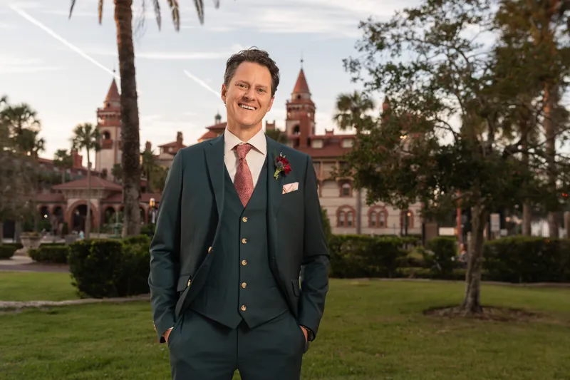 Rhett poses alone on the manicured grounds with the Spanish Renaissance architecture framing him behind.