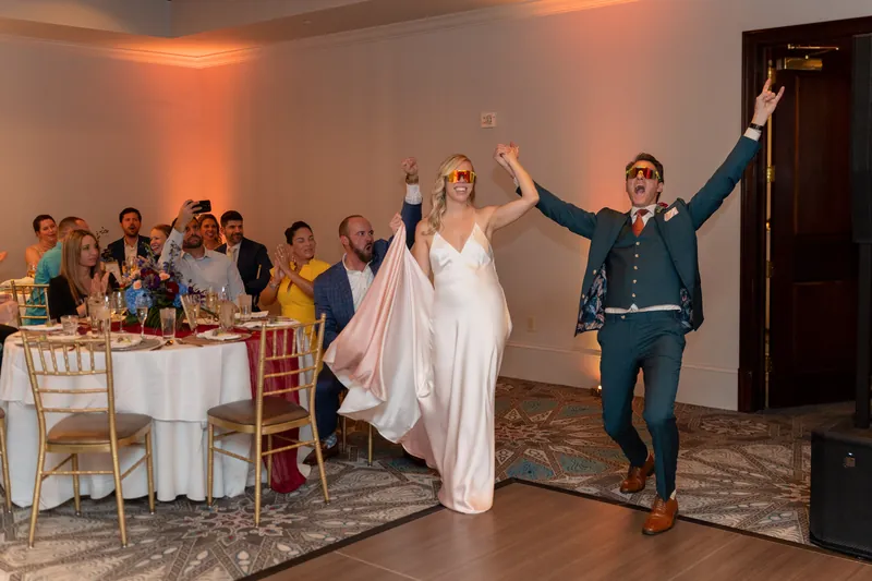 Kerry and Rhett raise their joined hands triumphantly as guests cheer around the reception ballroom.
