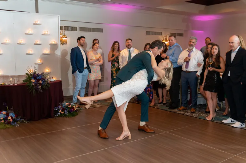 Kerry lifts one leg behind them in a playful backbend while dancing with Rhett on the ballroom floor surrounded by guests.