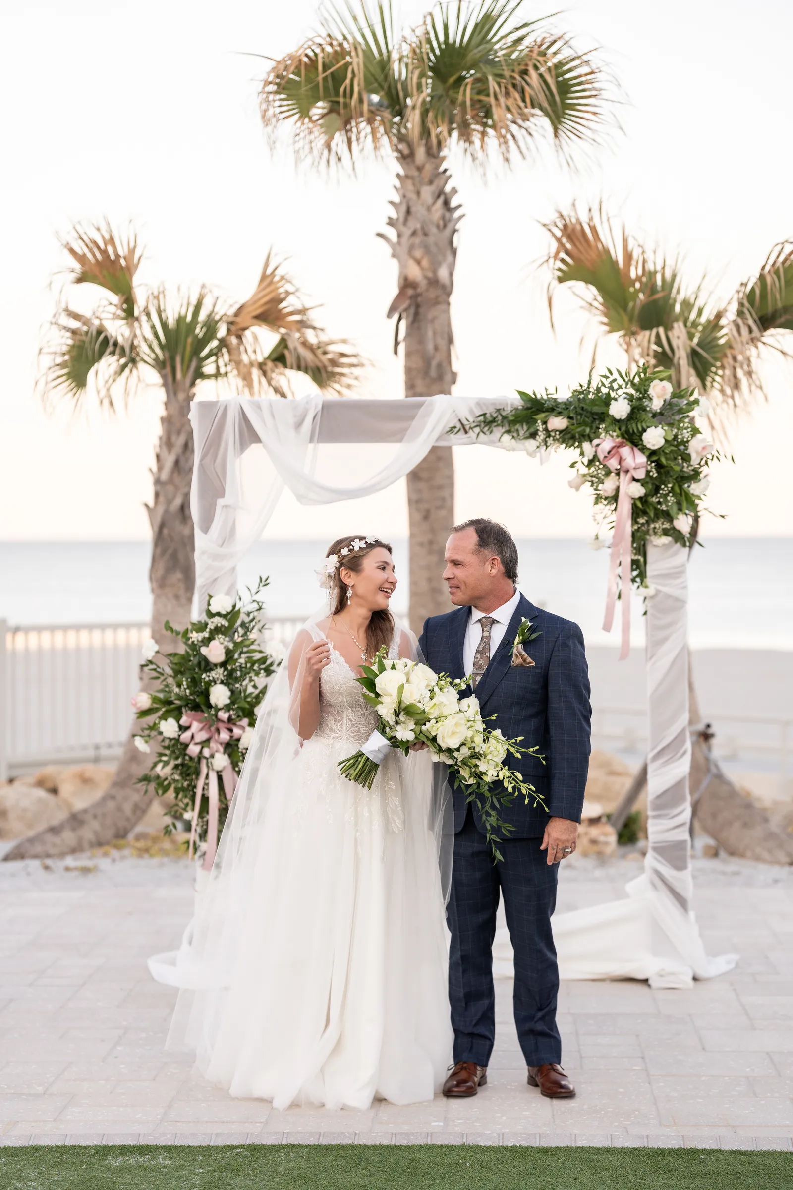 Bride and groom standing together at beachfront wedding ceremony under palm trees