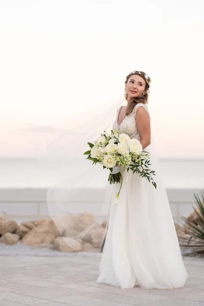 Bride in white dress holding white bouquet at beach sunset