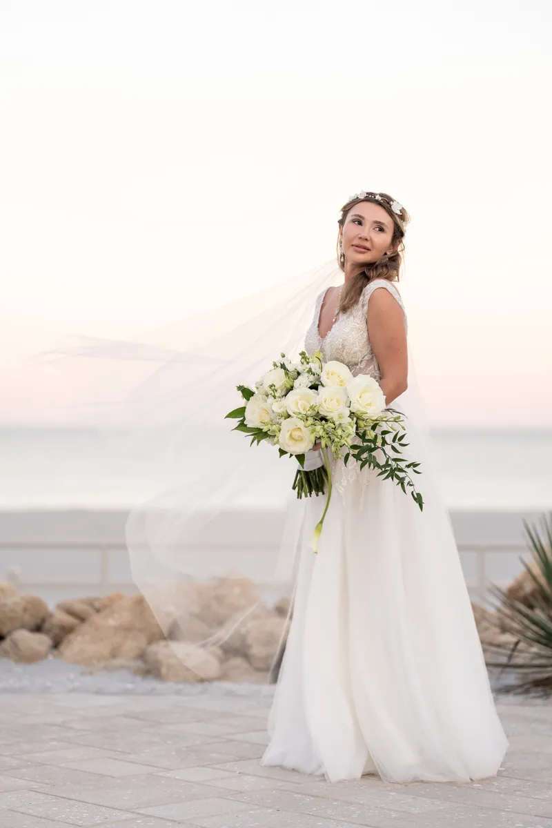 Bride in white dress holding white bouquet at beach sunset