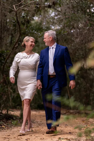 Kiley and Stacey walk hand-in-hand through dappled sunlight under a canopy of trees at Fort Mose.