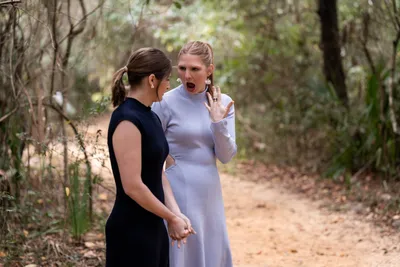 Two women conversing on wooded forest path during outdoor event