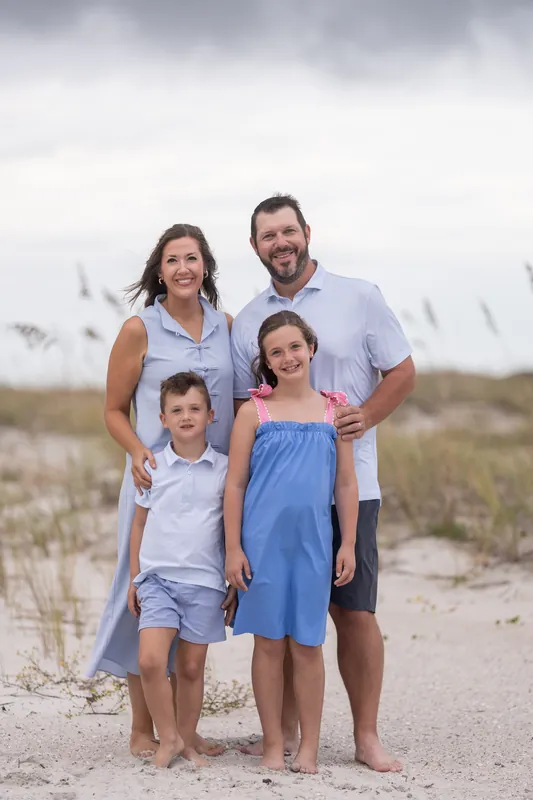 Four people in blue and white clothing stand close together on sand under gray skies at Vilano Beach.