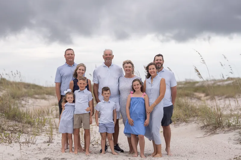 A group of eight people wearing light blue and white clothing gather on the sand at Vilano Beach, with dunes and sea oats framing the scene.