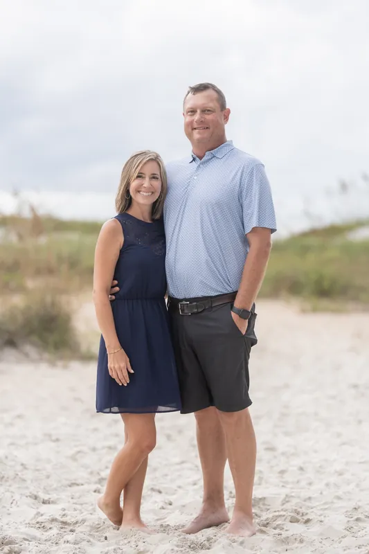 Two adults stand together on the beach at Vilano Beach, the man in a light blue shirt and the woman in a navy dress.