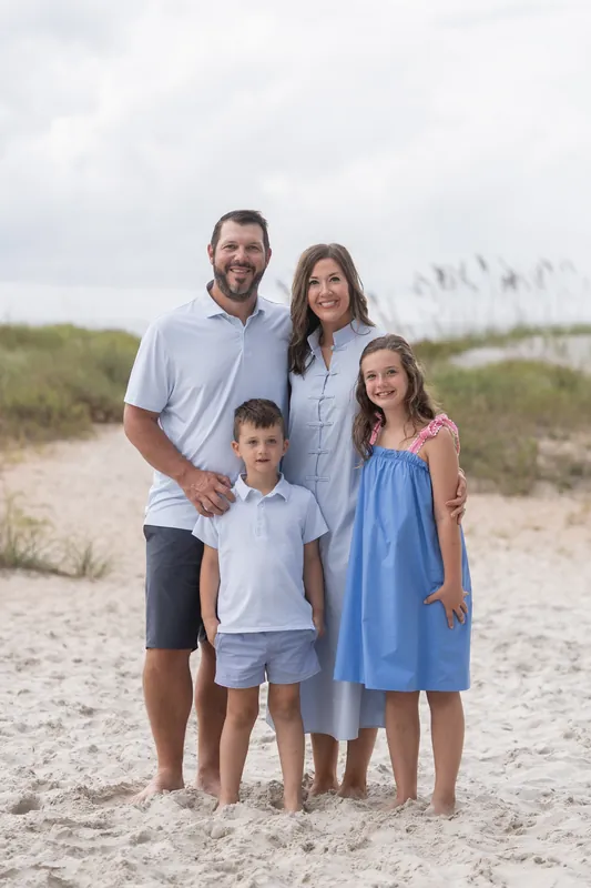 Parents and two children stand in casual beach attire on the sand with dune grasses visible behind them at Vilano Beach.