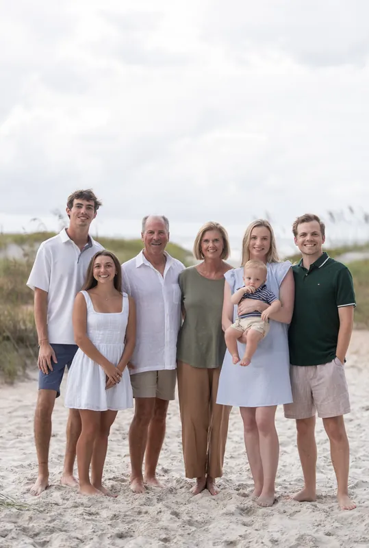 Eight people stand together on the beach at Vilano Beach, dressed in neutral tones, with sea oats visible along the shoreline.