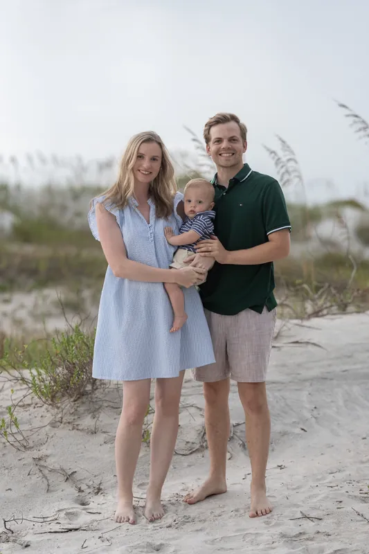 Two adults and a toddler stand on sand dunes at Vilano Beach, the child held between them.