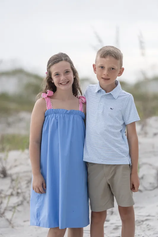 A girl in a blue and pink dress stands beside a boy in a light blue shirt on the beach at Vilano Beach.