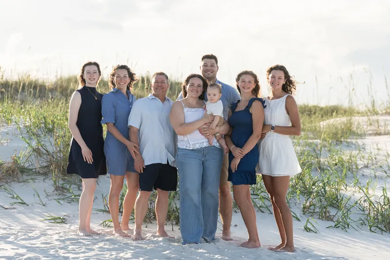 Extended family of eight stands together on the sand at St. Augustine Beach in casual summer clothing.