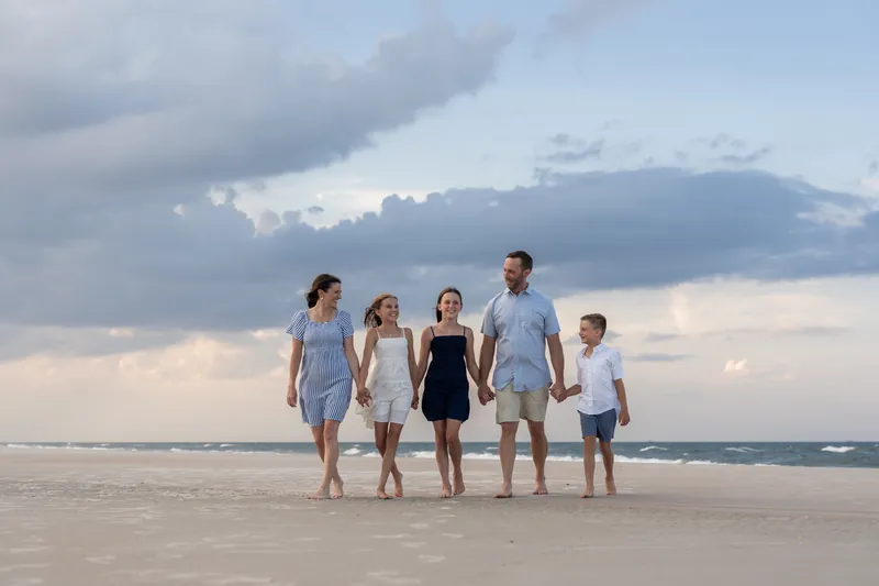 Five family members walk hand-in-hand along the shoreline at St. Augustine Beach as clouds gather overhead.
