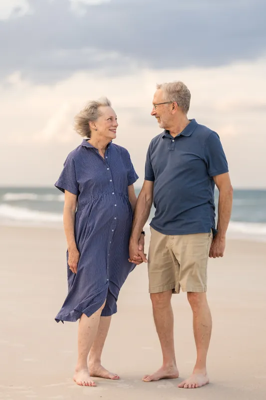 Kimberly and her husband hold hands at St. Augustine Beach, both wearing navy blue casual wear while gazing at each other