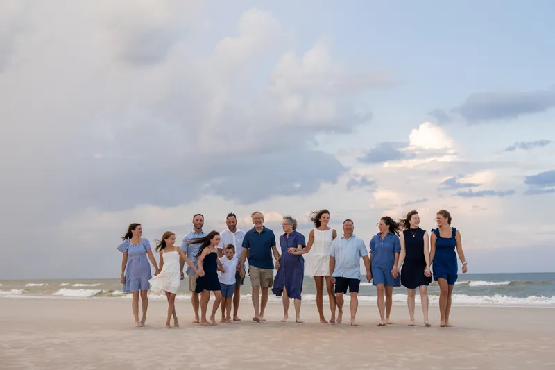A group of about fifteen people in casual summer clothing forms a line on the sand at St. Augustine Beach, standing together