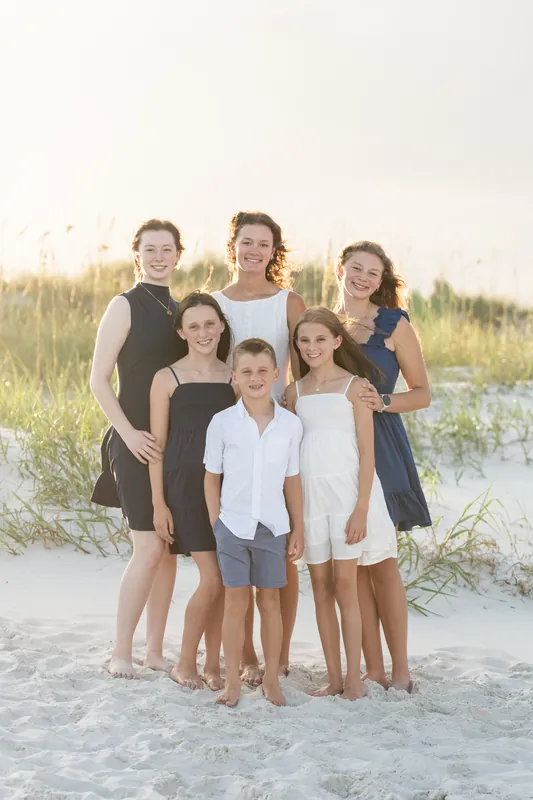 Fifteen people of varying ages line up across the wet sand facing the camera with the ocean and dramatic sky at St. Augustine