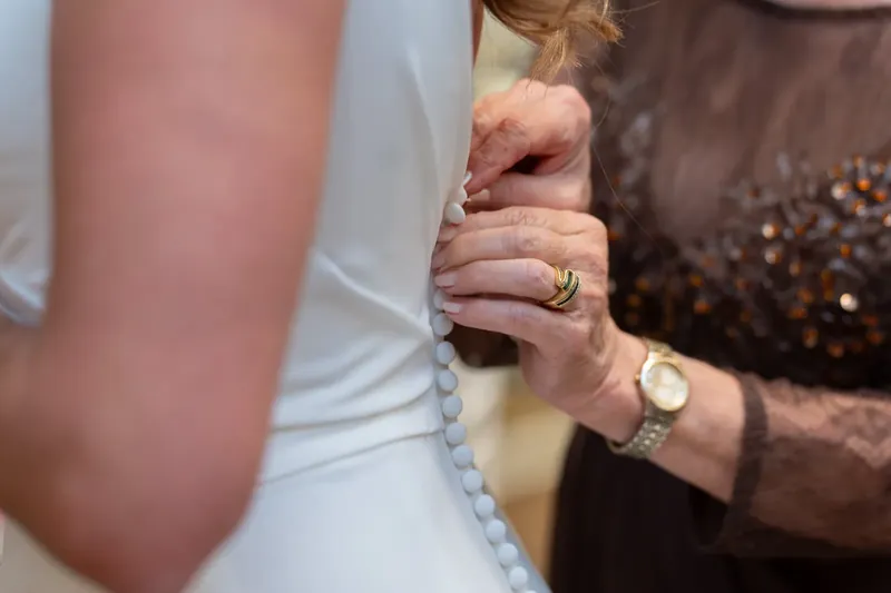Two people clasp hands at River House Events, their wedding bands visible as they stand together in a white dress and brown
