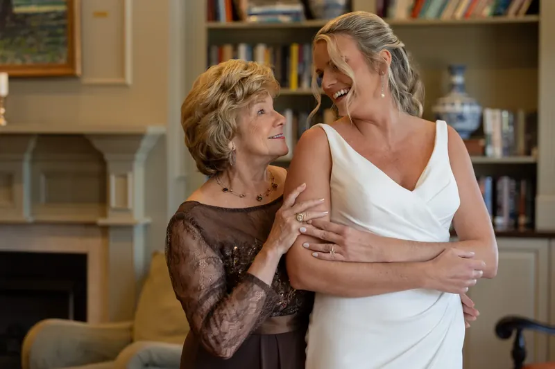 Kimberly embraces an older woman in a brown lace dress while laughing together in an elegant indoor room at River House
