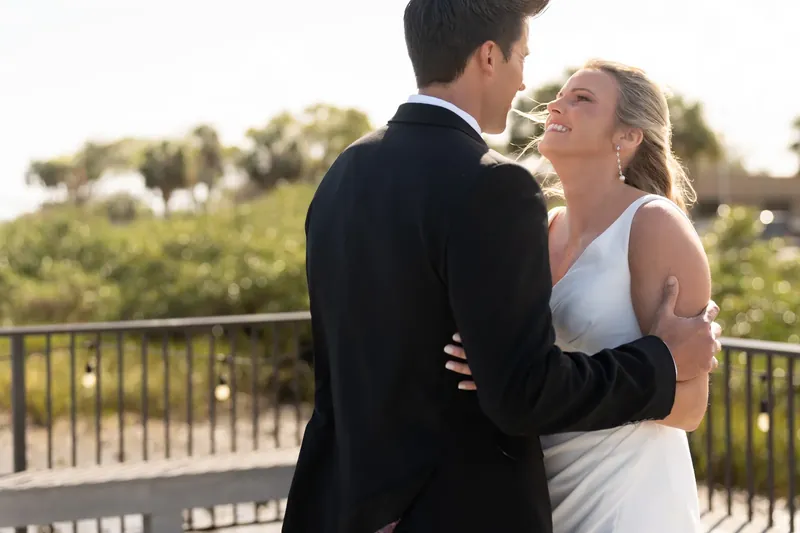 Landon and Kimberly embrace and laugh on a wooden deck with marsh views behind them.