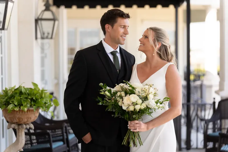 Kimberly gazes up at Landon while holding her bouquet on the venue's elegant covered terrace.