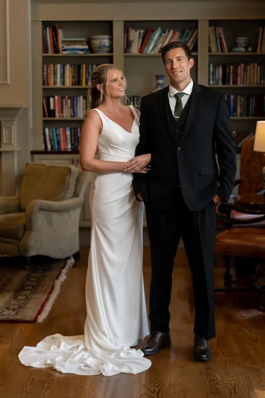 Kimberly and Landon stand together in the library room, her hand linked through his arm.