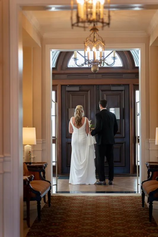 The couple stands in a doorway beneath a chandelier, framed by classical architectural details at the venue.