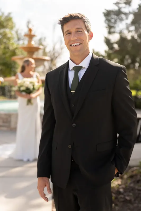 Landon smiles at the camera in a black suit and blue tie, with the venue's fountain visible behind him.