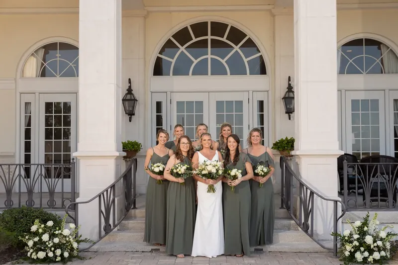 Kimberly stands center in a white dress surrounded by bridesmaids in sage green on the columned portico.