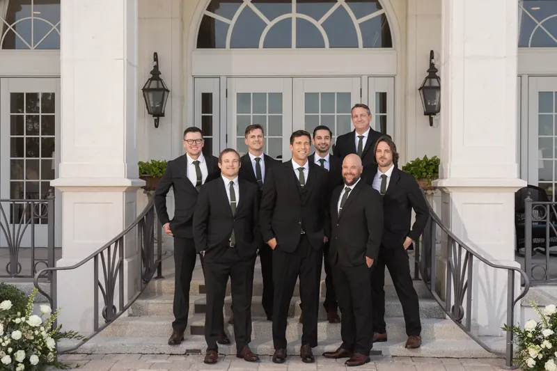 Landon and groomsmen in black suits pose together on the steps in front of white columns and planters.