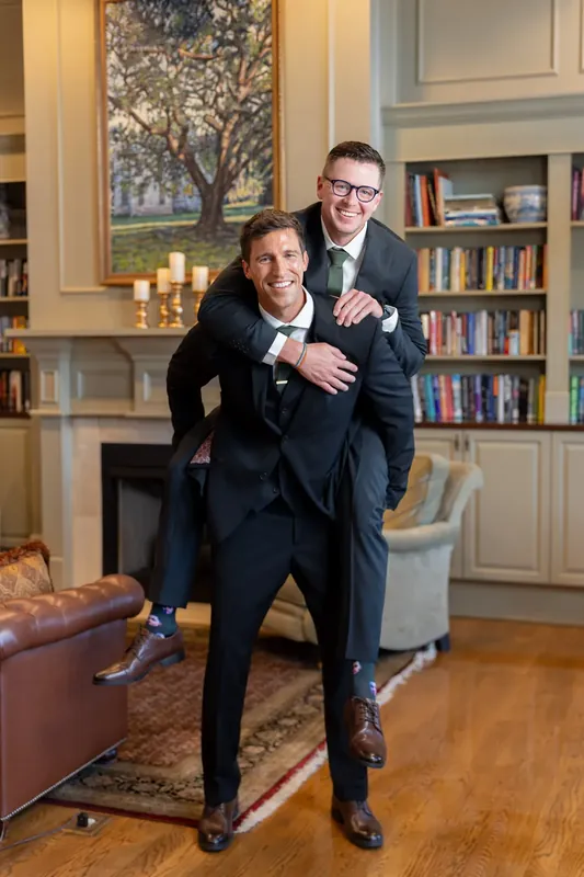 Landon grins while Kimberly hugs him from behind in River House Events' library lined with built-in bookshelves and candlelit