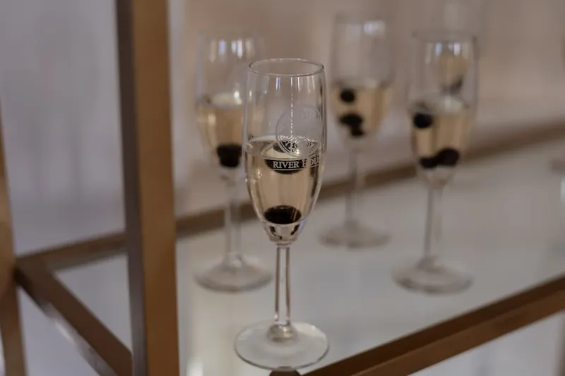 Champagne flutes filled with sparkling cider line a white table at River House Events, ready for the celebration.