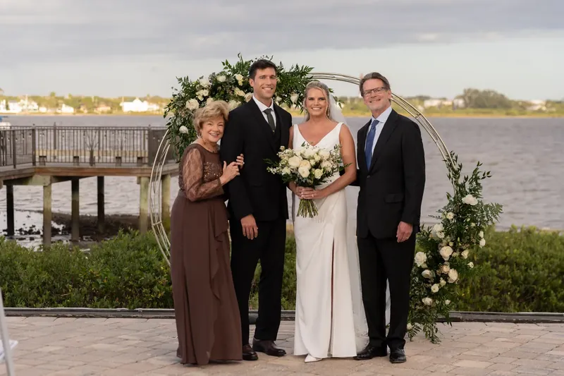 Kimberly and Landon pose with family members in front of a floral arch overlooking the river at River House Events.