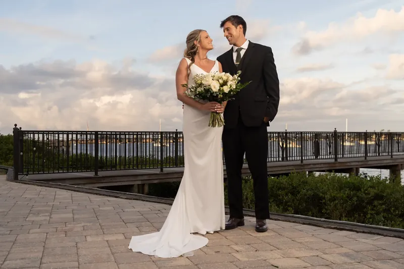 Kimberly and Landon stand together on the waterfront deck at River House Events, with Kimberly's white gown trailing behind
