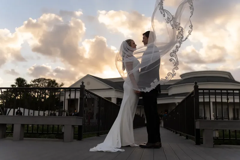 Landon lifts Kimberly as her veil swirls around them on a waterfront deck at sunset.
