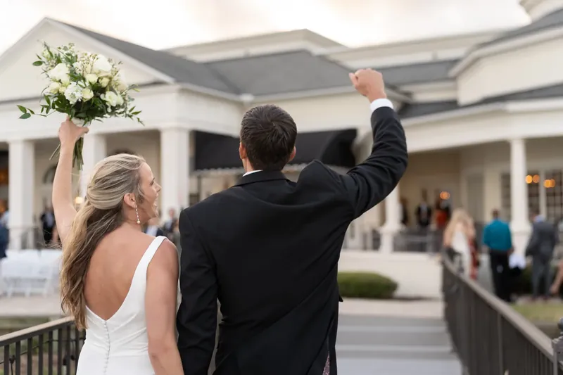 Landon raises his fist in celebration while holding Kimberly's bouquet as she looks back at the venue.