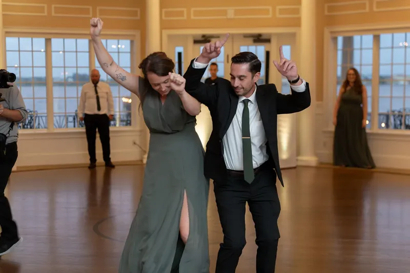 Kimberly and Landon dance with raised arms in the ballroom, surrounded by guests at River House Events, St. Augustine.