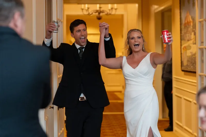 Landon and Kimberly raise their arms in celebration as they enter the ballroom at River House Events, with guests visible