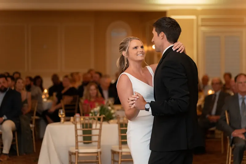 Landon kisses Kimberly's cheek during their first dance while seated guests watch from the reception hall.