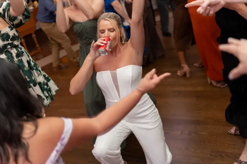 Kimberly, wearing a white strapless top, laughs and dances surrounded by wedding guests.