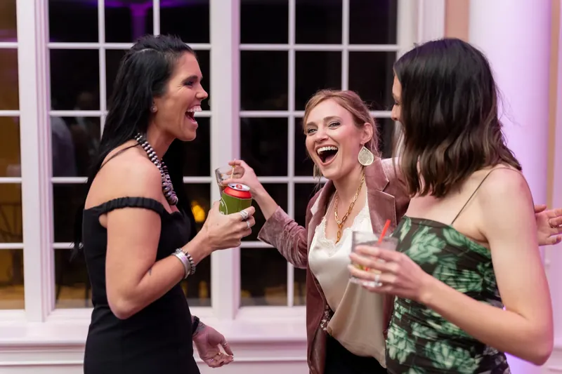 Three women clink champagne glasses and laugh together during the reception.