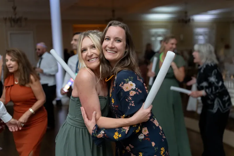 Two women embrace and smile while holding rolled programs at the reception.