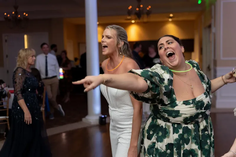 Two women dance with arms outstretched, laughing with joy on the dance floor.